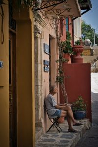 An old man sits on a chair in front of his house and looks down the street, surrounded by colorful houses