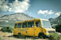 a yellow old school bus stands in the midday heat