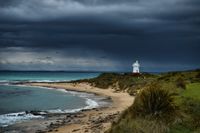 a bay, beach with a view of a white lighthouse. A dark blue storm front approaches