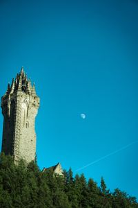 A monument touches the blue-turquoise sky, which is already letting the moon shine through